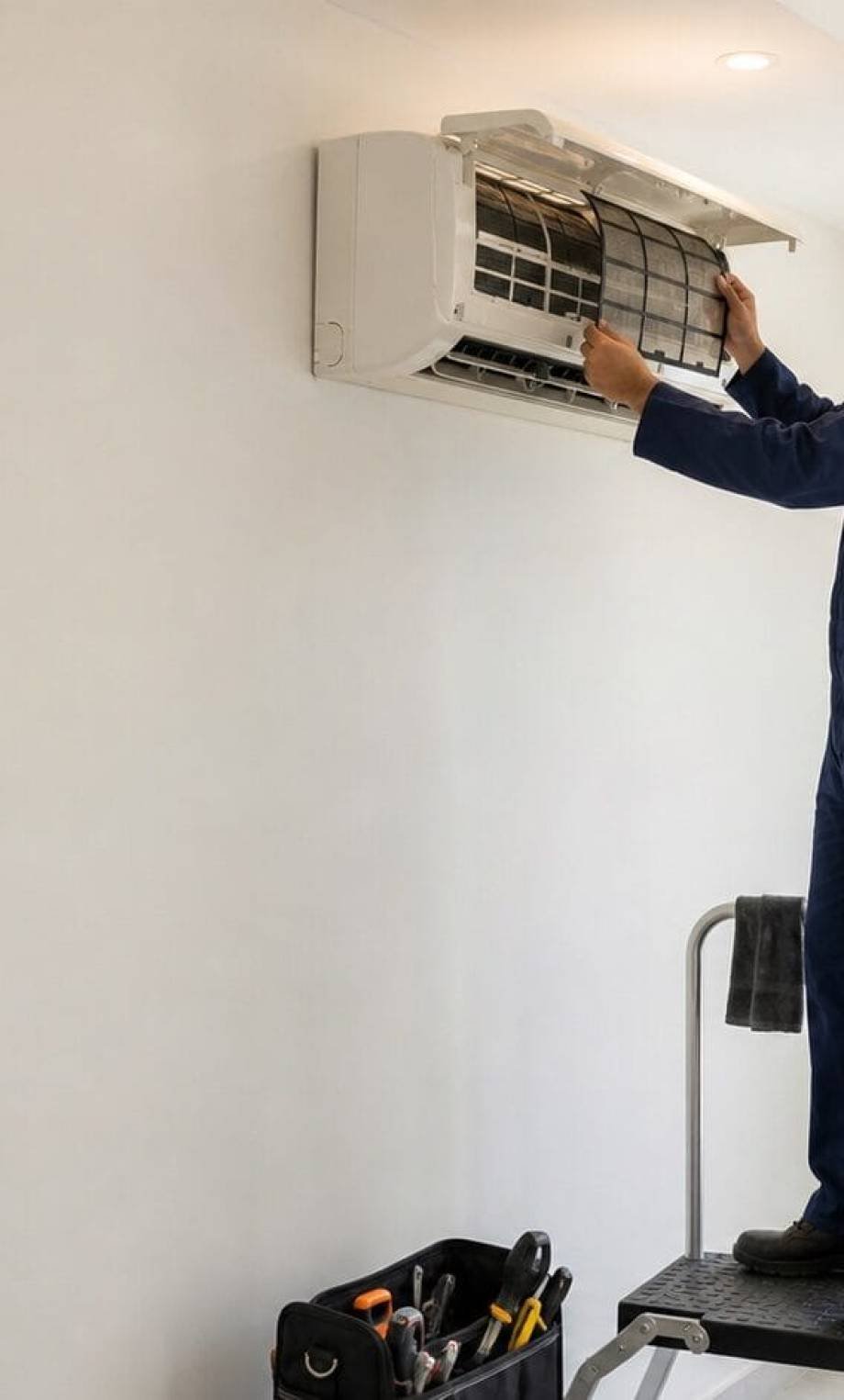 Technician servicing an indoor wall-mounted AC unit during a maintenance visit